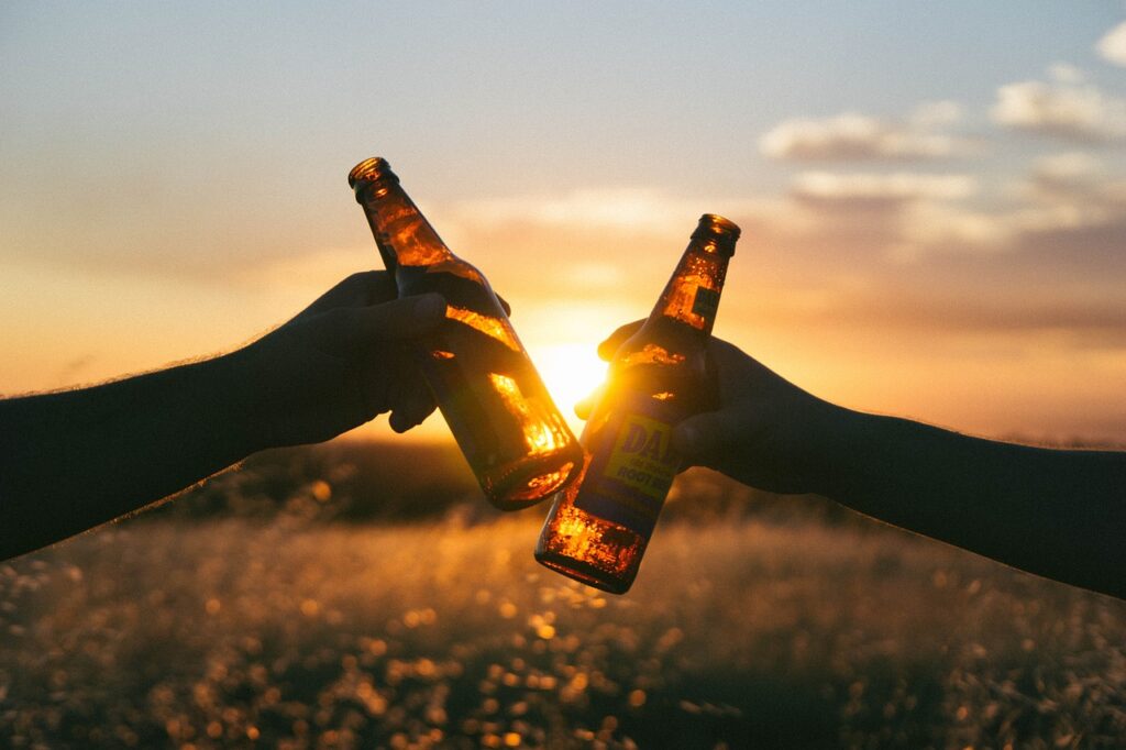 Deux mains qui tiennent une bière et qui trinquent devant le coucher du soleil
